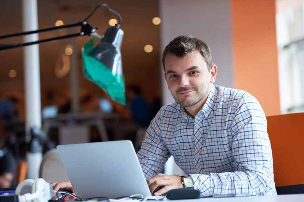 Man at desk smiling at camera wearing checked shirt