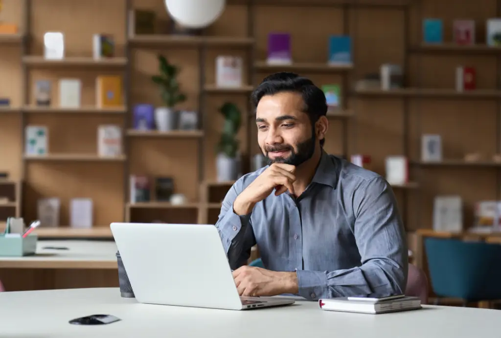 A man at a table with a laptop, smiling as he efficiently manages membership software in his office.