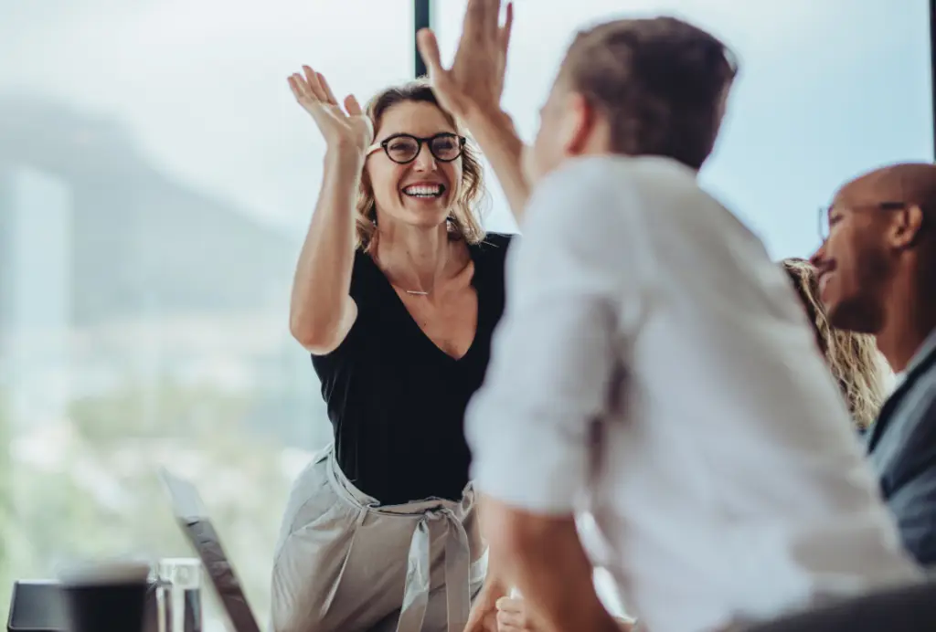 A woman joyfully raises her hands at a table with colleagues, celebrating their successful membership operation.