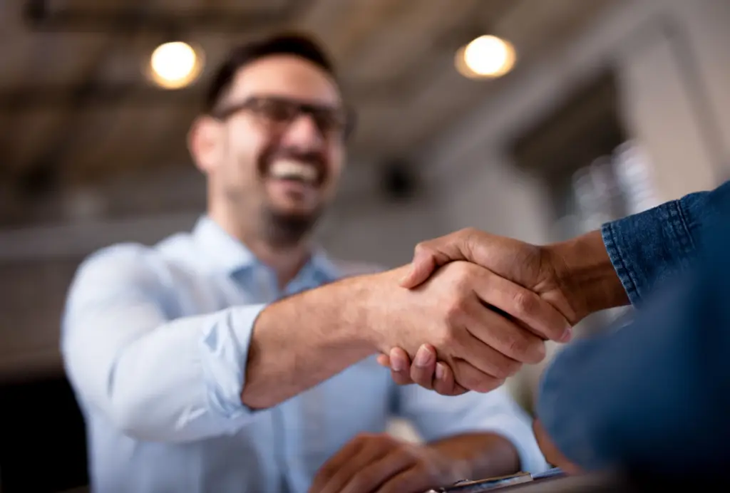 Man smiling, shaking hands with client in office environment.