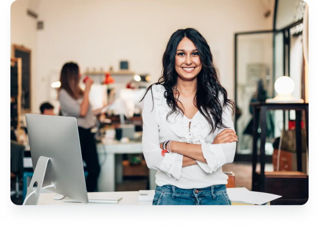 A smiling entrepreneur stands confidently with arms crossed in front of her desk, celebrating her business success with Dynamics 365.